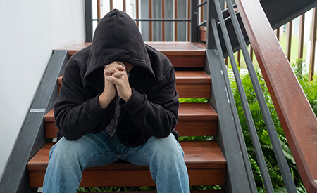 Depressed man in black hoodie sitting on stairs