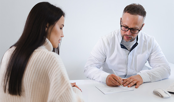 Male doctor writing a prescription for female medication management patient